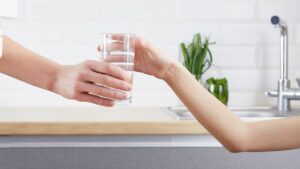 Parent handing child a glass of water cleaned by whole house water filter installation in Houston