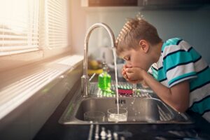 Child drinking water from sink with reverse osmosis water filter. 