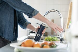 Person filling water bottle after getting a carbon water filter system for the home